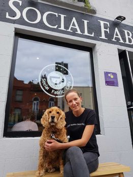 A staff member with a dog outside a Social Fabric Café 