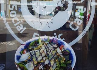 Social Fabric Café logo on glass with a delicious salad from our menu